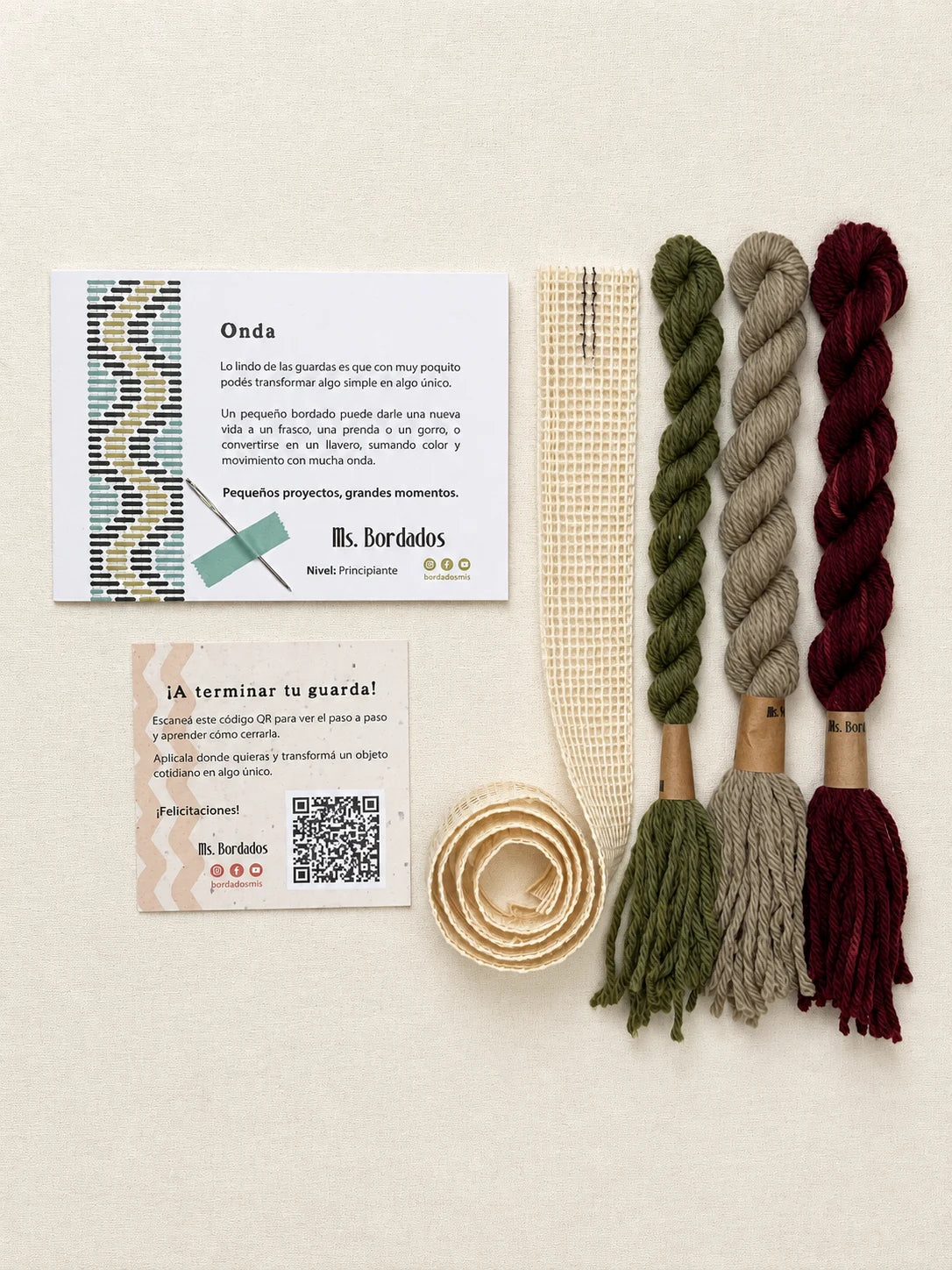 Componentes del Kit Franja Onda Huerta (formato Guarda larga): cañamazo de 75 × 5 cm, lanas 100% uruguayas en Verde seco, Verde eucaliptus y Berenjena, aguja, manual impreso y tarjeta con el QR del video para terminar tu guarda — Ms. Bordados