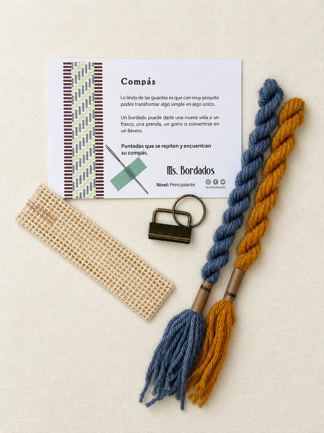 Componentes del Kit Franja Compás Provenza (formato Llavero): cañamazo, lanas 100% uruguayas en Celeste y Amarillo, aguja, manual impreso y herraje del llavero — Ms. Bordados
