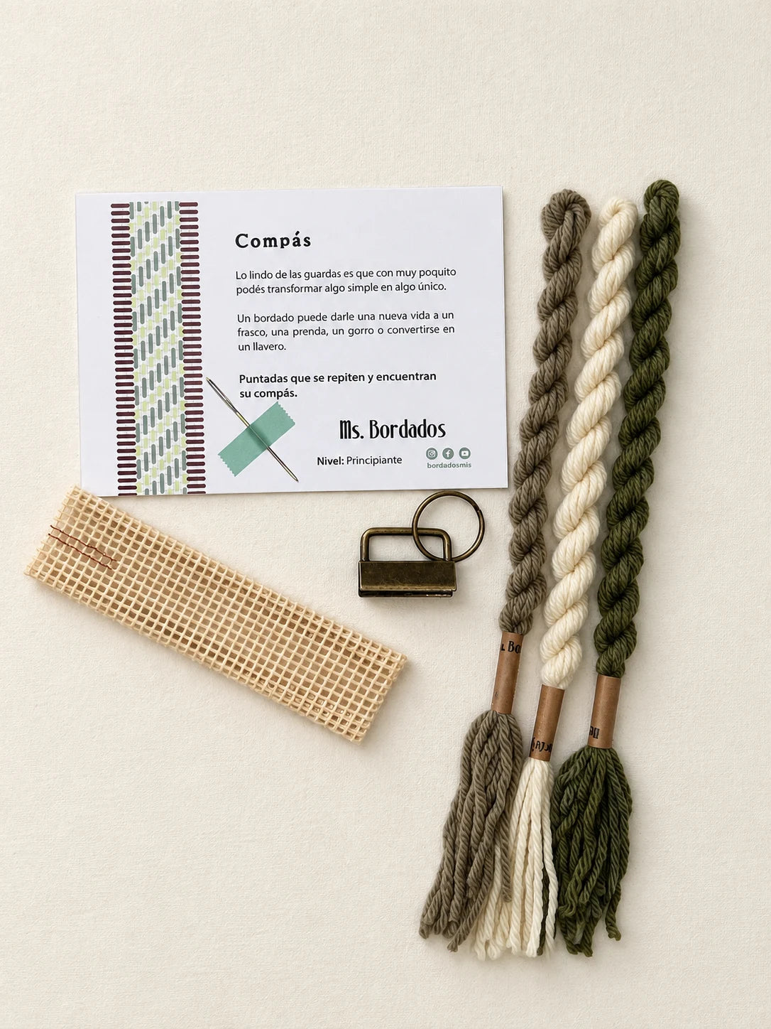 Componentes del Kit Franja Compás Salvia (formato Llavero): cañamazo, lanas 100% uruguayas en Crudo, Verde seco y Taupe, aguja, manual impreso y herraje del llavero — Ms. Bordados