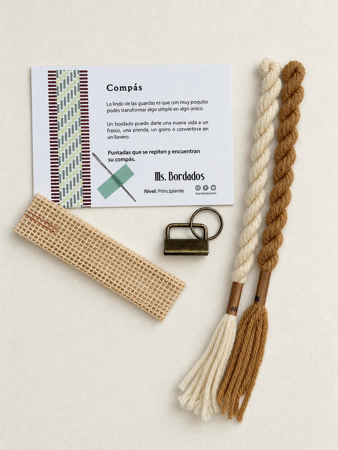 Componentes del Kit Franja Compás Sol (formato Llavero): cañamazo, lanas 100% uruguayas en Crudo y Dijon, aguja, manual impreso y herraje del llavero — Ms. Bordados