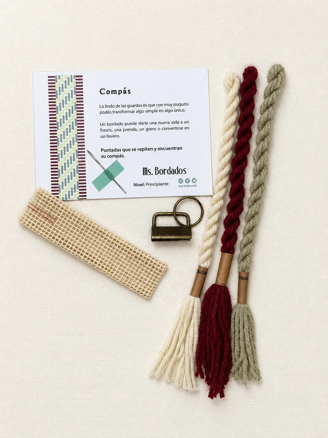 Componentes del Kit Franja Compás Viñedo (formato Llavero): cañamazo, lanas 100% uruguayas en Crudo, Verde eucaliptus y Bordeaux, aguja, manual impreso y herraje del llavero — Ms. Bordados