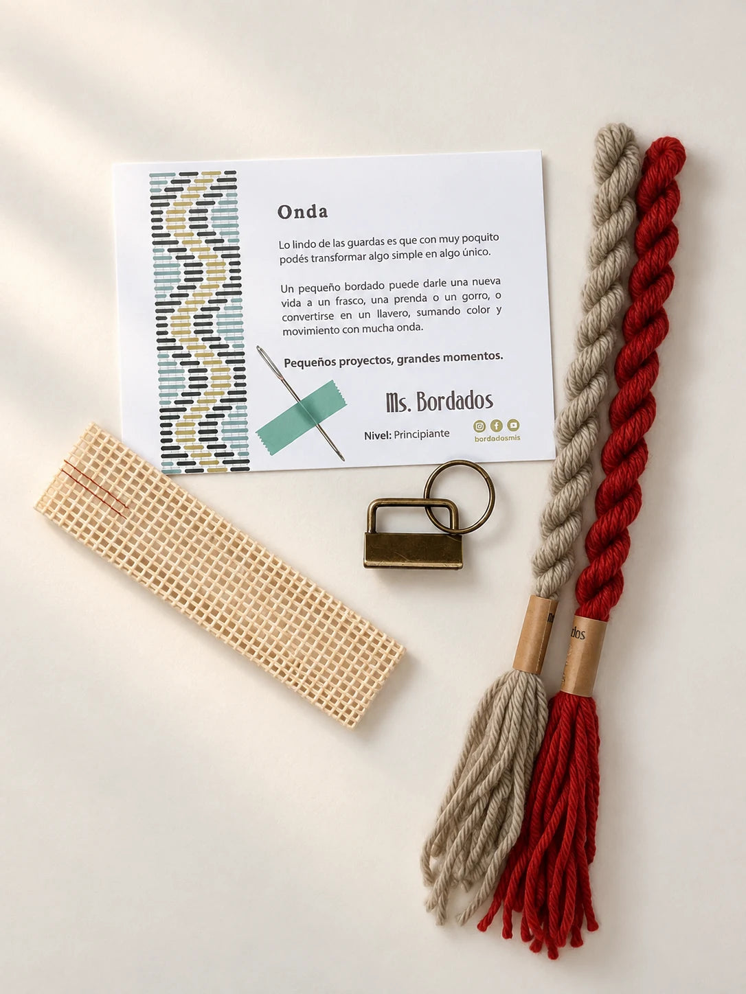 Componentes del Kit Franja Onda Amapola (formato Llavero): cañamazo, lanas 100% uruguayas en Verde eucaliptus y Rojo, aguja, manual impreso y herraje del llavero — Ms. Bordados