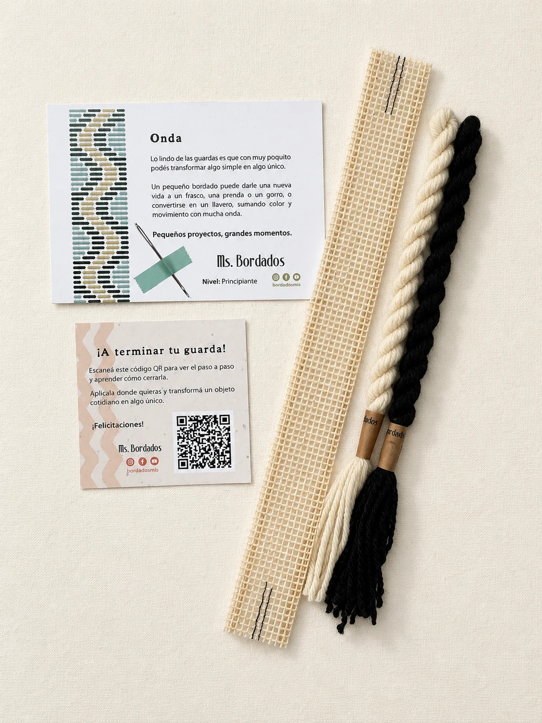 Componentes del Kit Franja Onda Cebra (formato Guarda corta): cañamazo de 30 × 5 cm, lanas 100% uruguayas en Negro y Crudo, aguja, manual impreso y tarjeta con el QR del video para terminar tu guarda — Ms. Bordados