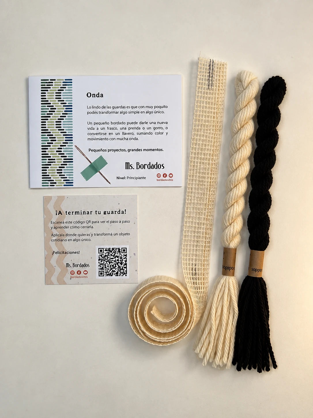 Componentes del Kit Franja Onda Cebra (formato Guarda larga): cañamazo de 75 × 5 cm, lanas 100% uruguayas en Negro y Crudo, aguja, manual impreso y tarjeta con el QR del video para terminar tu guarda — Ms. Bordados