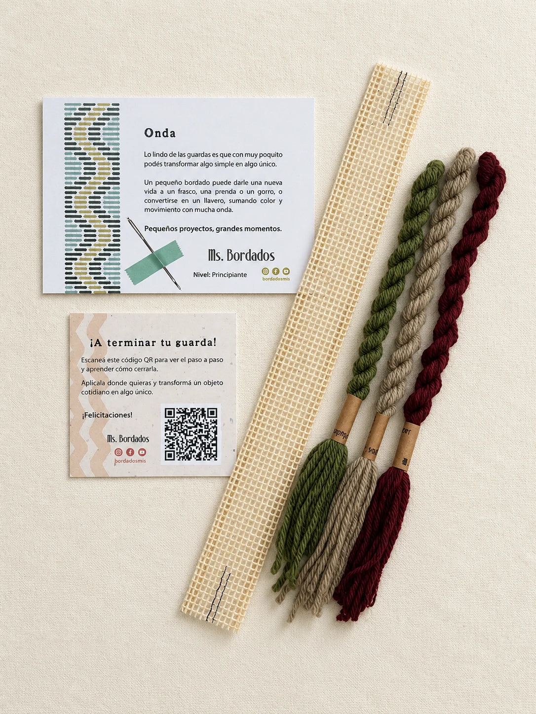 Componentes del Kit Franja Onda Huerta (formato Guarda corta): cañamazo de 30 × 5 cm, lanas 100% uruguayas en Verde seco, Verde eucaliptus y Berenjena, aguja, manual impreso y tarjeta con el QR del video para terminar tu guarda — Ms. Bordados