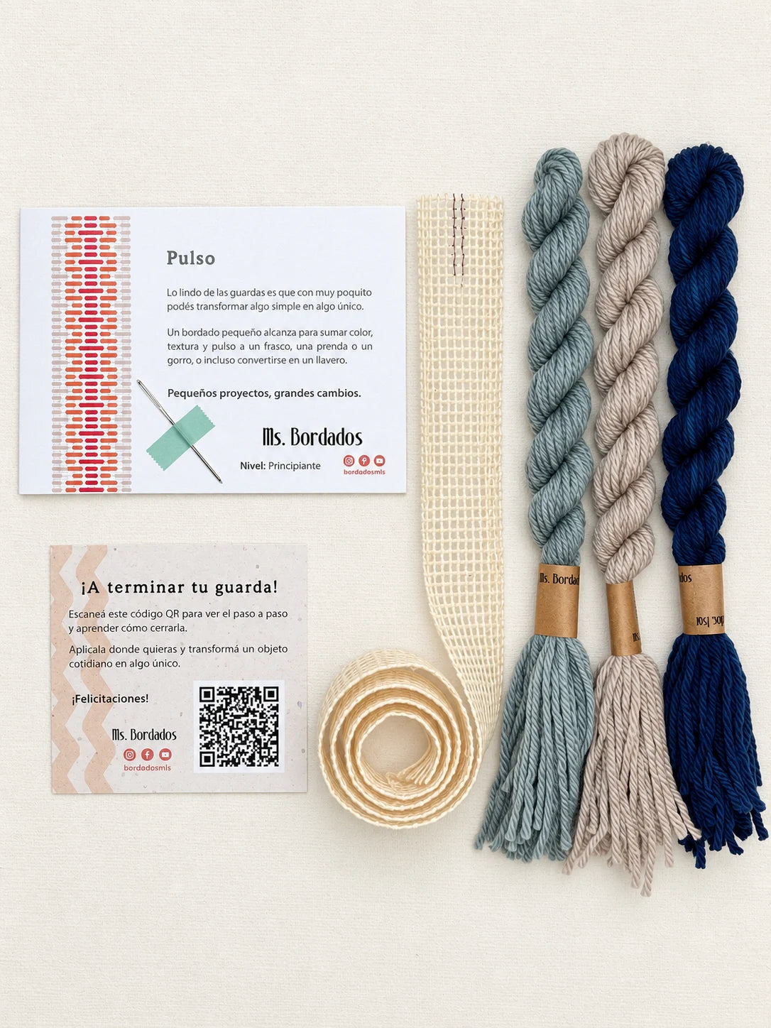 Componentes del Kit Franja Pulso Puerto (formato Guarda larga): cañamazo de 75 × 5 cm, lanas 100% uruguayas en Beige, Azul y Gris celeste, aguja, manual impreso y tarjeta con el QR del video para terminar tu guarda — Ms. Bordados