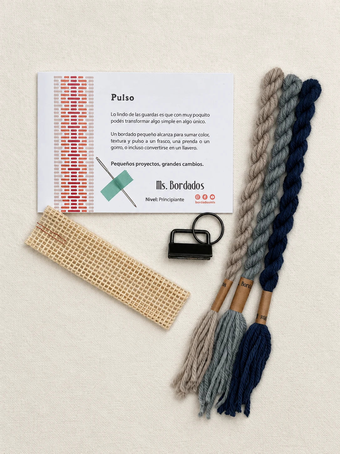 Componentes del Kit Franja Pulso Puerto (formato Llavero): cañamazo, lanas 100% uruguayas en Beige, Azul y Gris celeste, aguja, manual impreso y herraje del llavero — Ms. Bordados