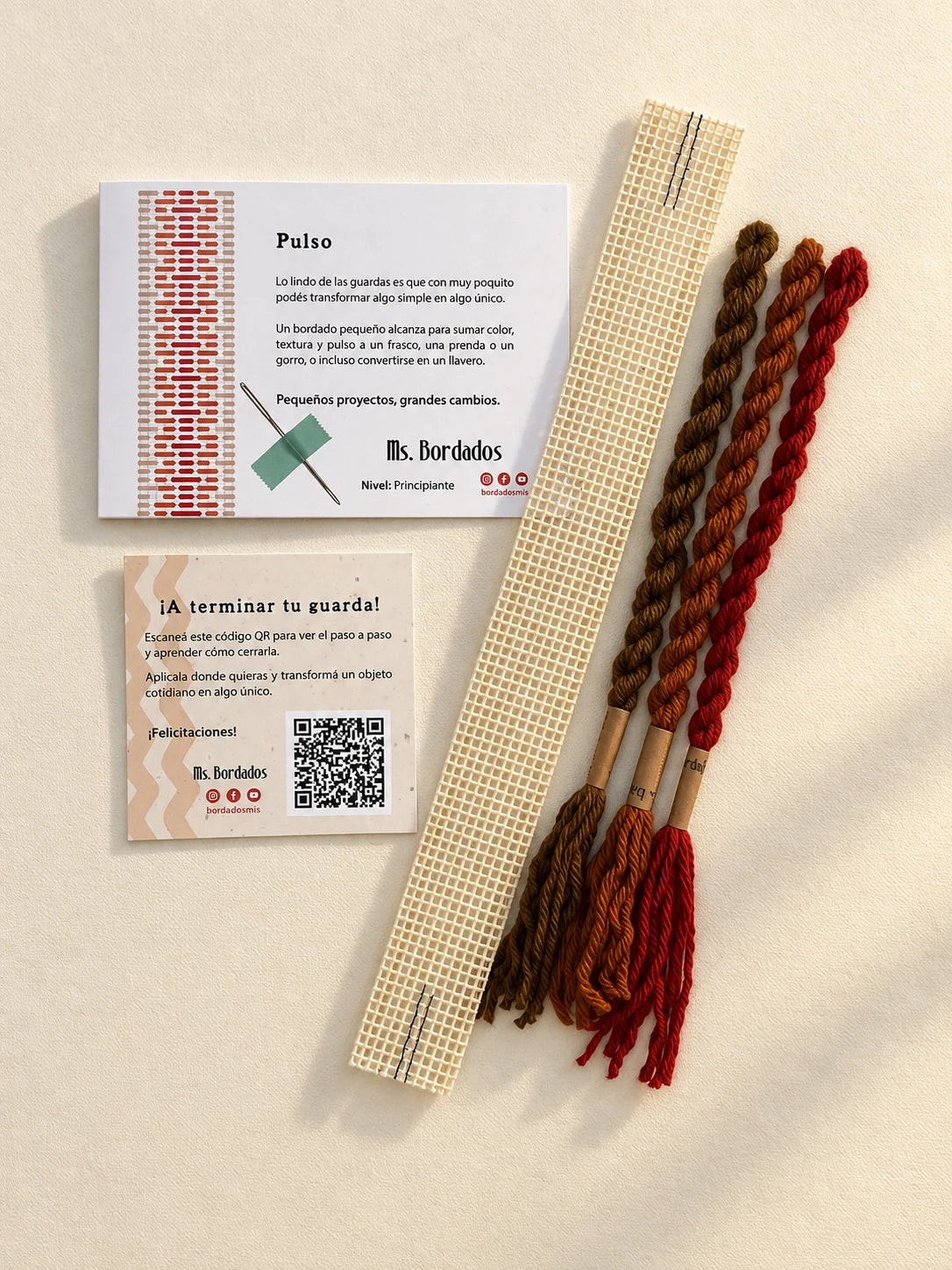 Componentes del Kit Franja Pulso Terracota (formato Guarda corta): cañamazo de 30 × 5 cm, lanas 100% uruguayas en Rojo ladrillo, Cobre y Tostado, aguja, manual impreso y tarjeta con el QR del video para terminar tu guarda — Ms. Bordados