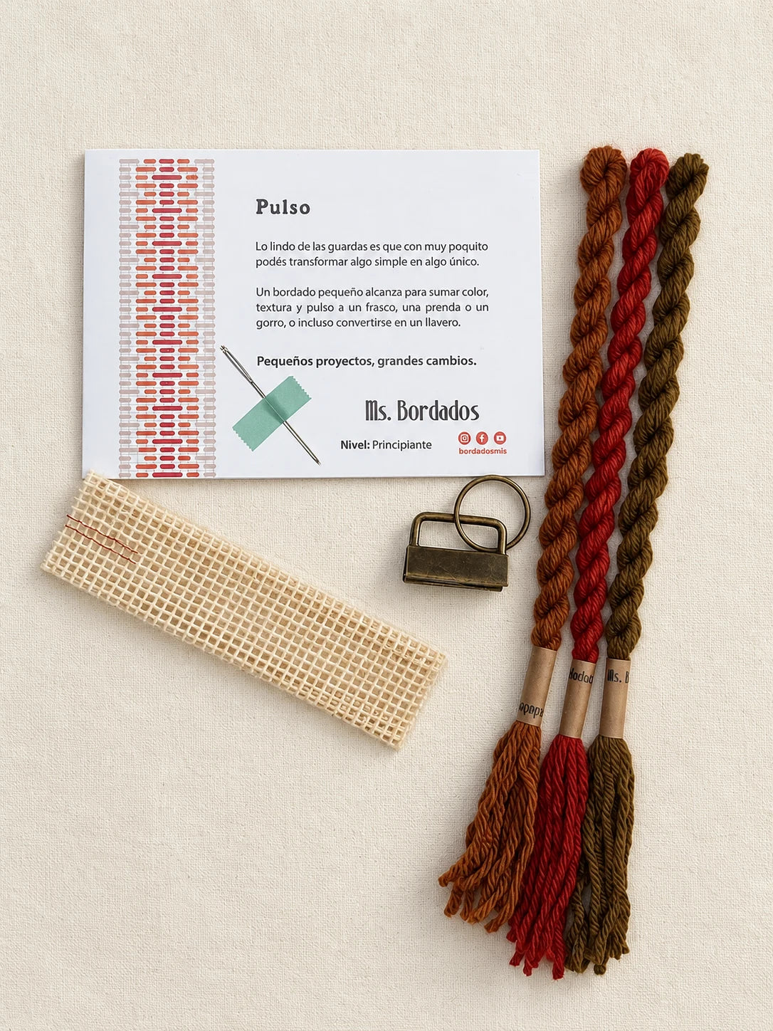 Componentes del Kit Franja Pulso Terracota (formato Llavero): cañamazo, lanas 100% uruguayas en Rojo ladrillo, Cobre y Tostado, aguja, manual impreso y herraje del llavero — Ms. Bordados