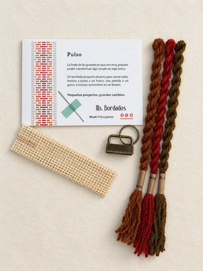 Componentes del Kit Franja Pulso Terracota (formato Llavero): cañamazo, lanas 100% uruguayas en Rojo ladrillo, Cobre y Tostado, aguja, manual impreso y herraje del llavero — Ms. Bordados