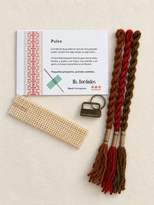 Componentes del Kit Franja Pulso Terracota (formato Llavero): cañamazo, lanas 100% uruguayas en Rojo ladrillo, Cobre y Tostado, aguja, manual impreso y herraje del llavero — Ms. Bordados