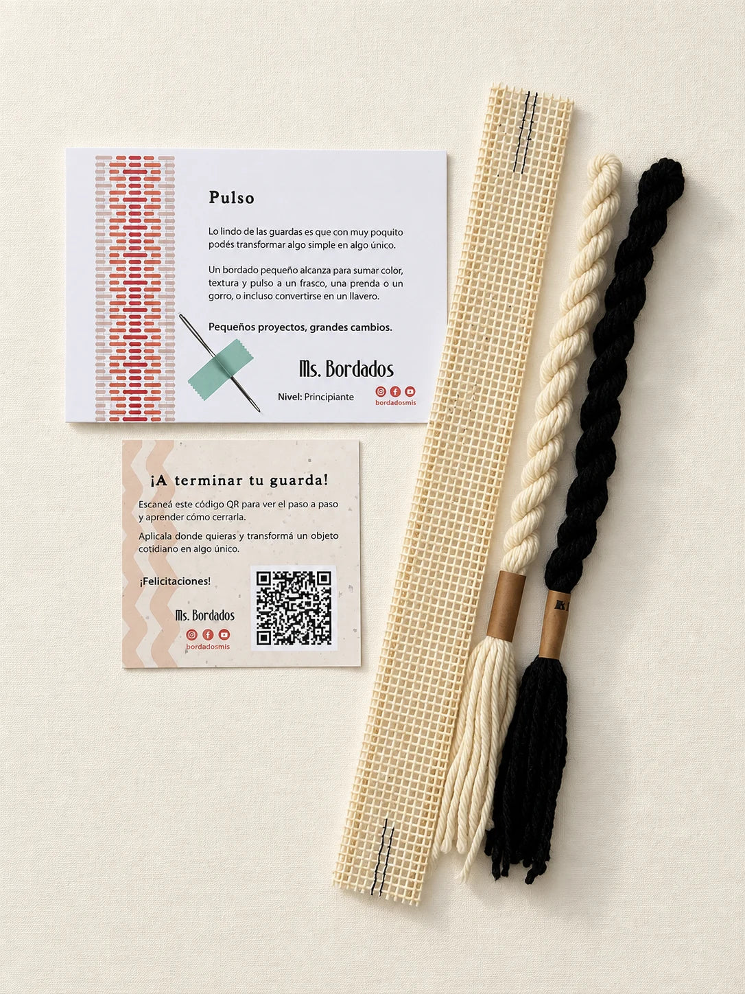 Componentes del Kit Franja Pulso Tinta (formato Guarda corta): cañamazo de 30 × 5 cm, lanas 100% uruguayas en Negro y Crudo, aguja, manual impreso y tarjeta con el QR del video para terminar tu guarda — Ms. Bordados