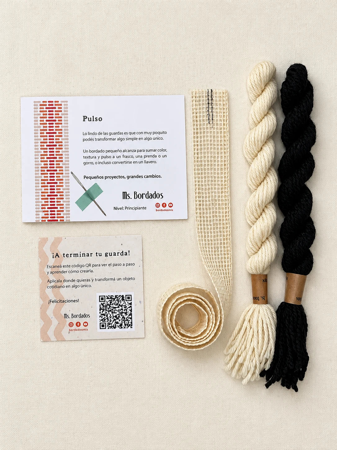 Componentes del Kit Franja Pulso Tinta (formato Guarda larga): cañamazo de 75 × 5 cm, lanas 100% uruguayas en Negro y Crudo, aguja, manual impreso y tarjeta con el QR del video para terminar tu guarda — Ms. Bordados