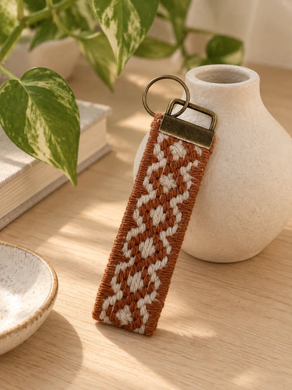 Llavero Franja Ritmo Cobre bordado sobre cañamazo, en Beige y Cobre, sobre una mesa — Ms. Bordados
