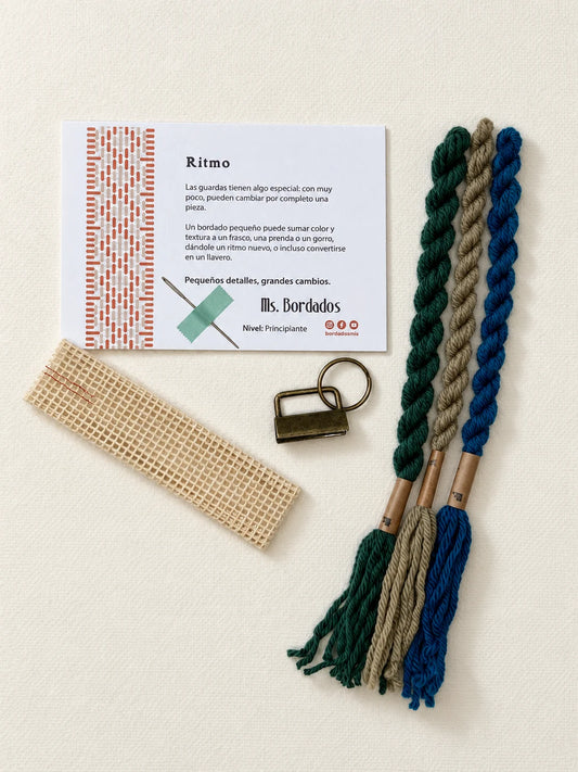 Componentes del Kit Franja Ritmo Pavo Real (formato Llavero): cañamazo, lanas 100% uruguayas en Azul eléctrico, Verde forestal y Taupe, aguja, manual impreso y herraje del llavero — Ms. Bordados