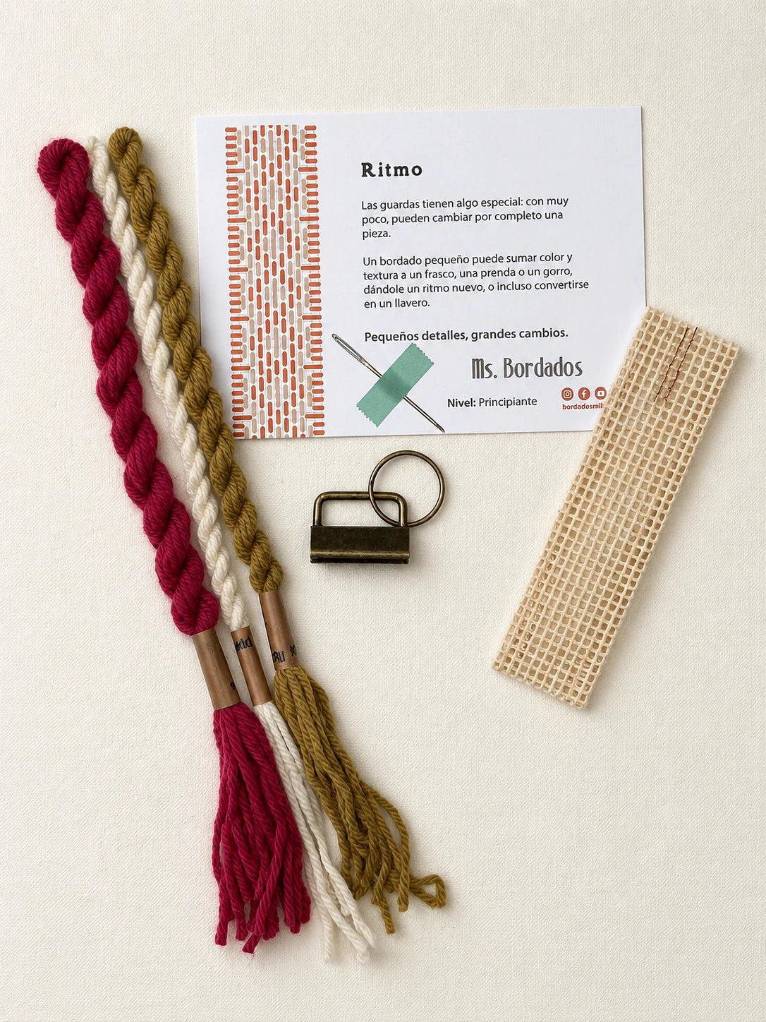 Componentes del Kit Franja Ritmo Vintage (formato Llavero): cañamazo, lanas 100% uruguayas en Magenta viejo, Oro viejo y Crudo, aguja, manual impreso y herraje del llavero — Ms. Bordados