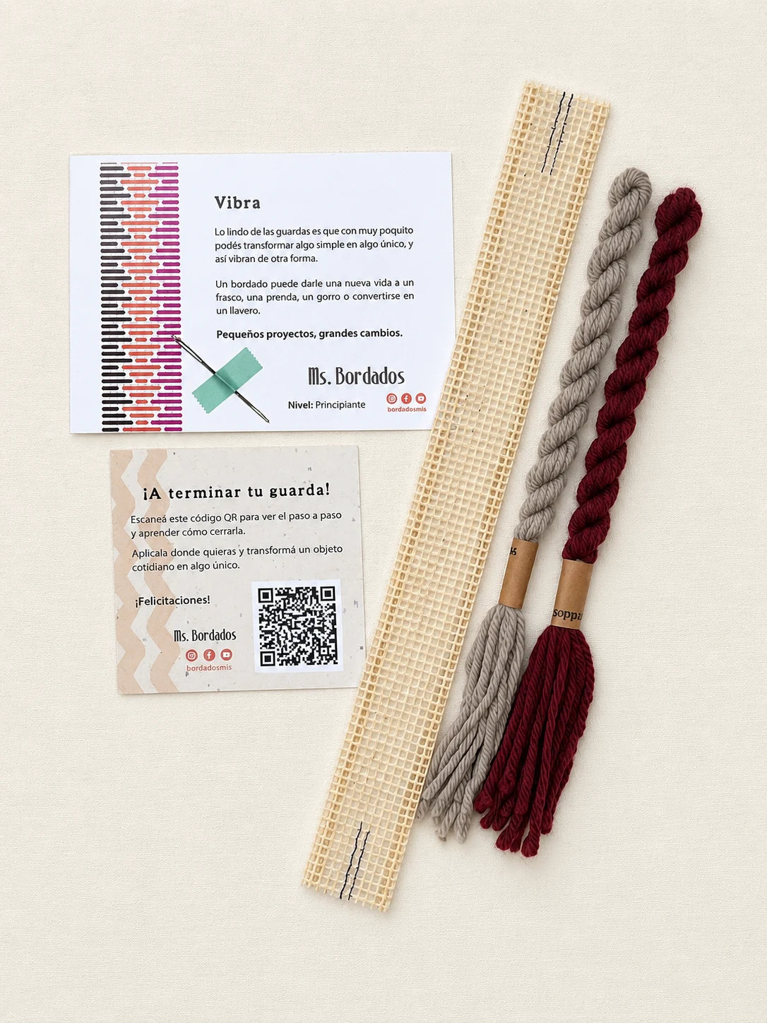 Componentes del Kit Franja Vibra Burdeos (formato Guarda corta): cañamazo de 30 × 5 cm, lanas 100% uruguayas en Bordeaux y Gris, aguja, manual impreso y tarjeta con el QR del video para terminar tu guarda — Ms. Bordados