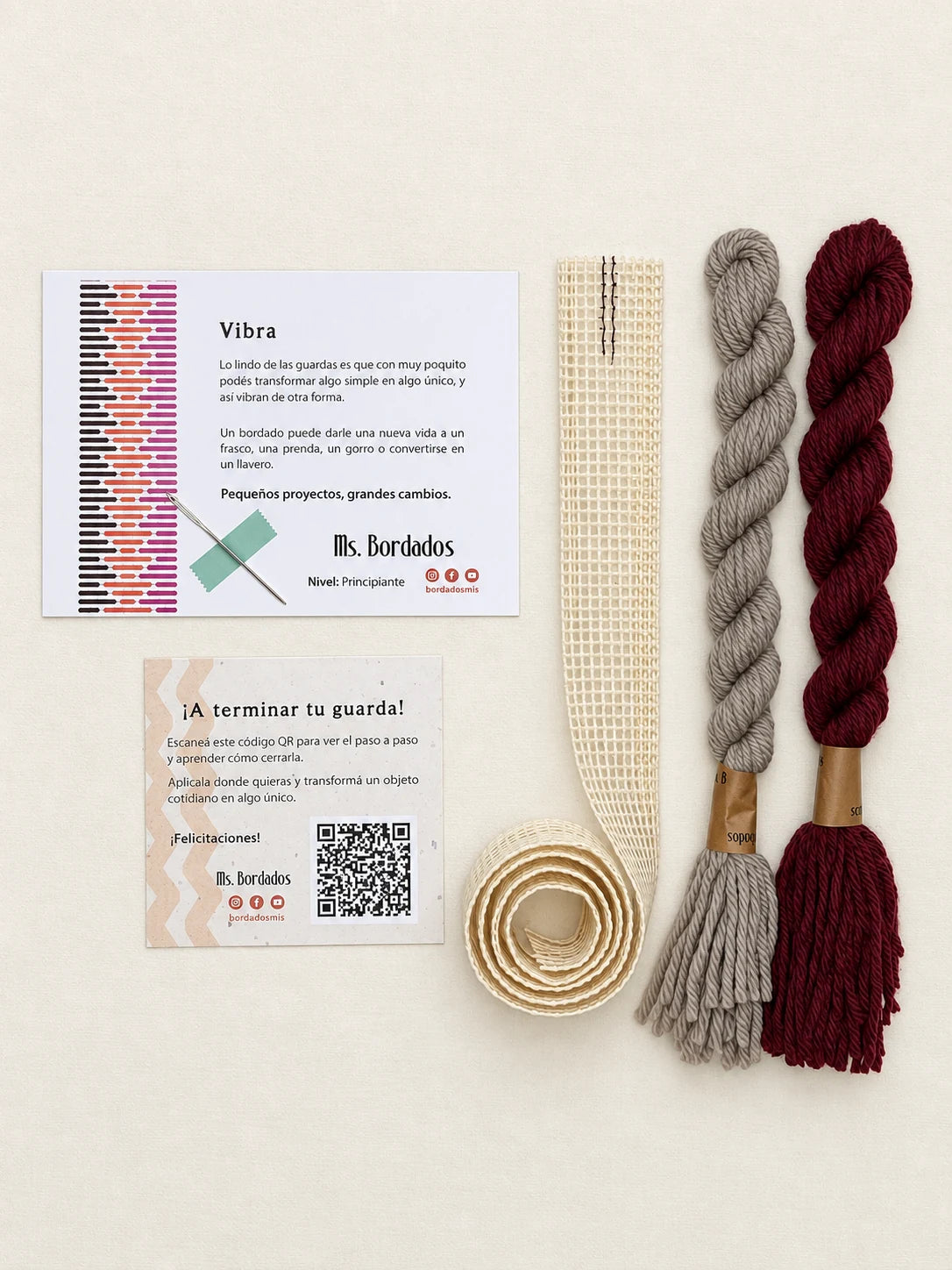 Componentes del Kit Franja Vibra Burdeos (formato Guarda larga): cañamazo de 75 × 5 cm, lanas 100% uruguayas en Bordeaux y Gris, aguja, manual impreso y tarjeta con el QR del video para terminar tu guarda — Ms. Bordados