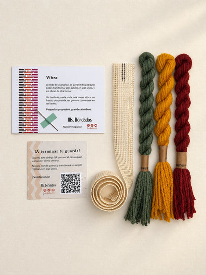 Componentes del Kit Franja Vibra Kilim (formato Guarda larga): cañamazo de 75 × 5 cm, lanas 100% uruguayas en Verde forestal, Rojo ladrillo y Amarillo, aguja, manual impreso y tarjeta con el QR del video para terminar tu guarda — Ms. Bordados