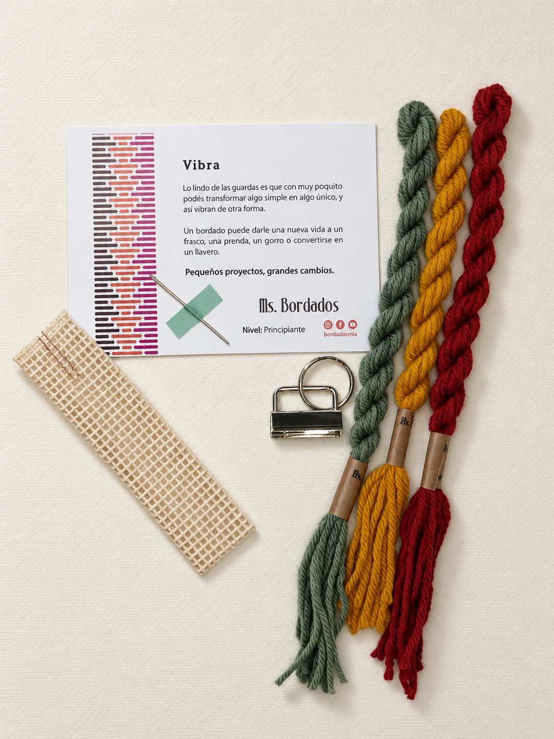 Componentes del Kit Franja Vibra Kilim (formato Llavero): cañamazo, lanas 100% uruguayas en Verde forestal, Rojo ladrillo y Amarillo, aguja, manual impreso y herraje del llavero — Ms. Bordados
