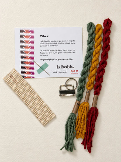 Componentes del Kit Franja Vibra Kilim (formato Llavero): cañamazo, lanas 100% uruguayas en Verde forestal, Rojo ladrillo y Amarillo, aguja, manual impreso y herraje del llavero — Ms. Bordados
