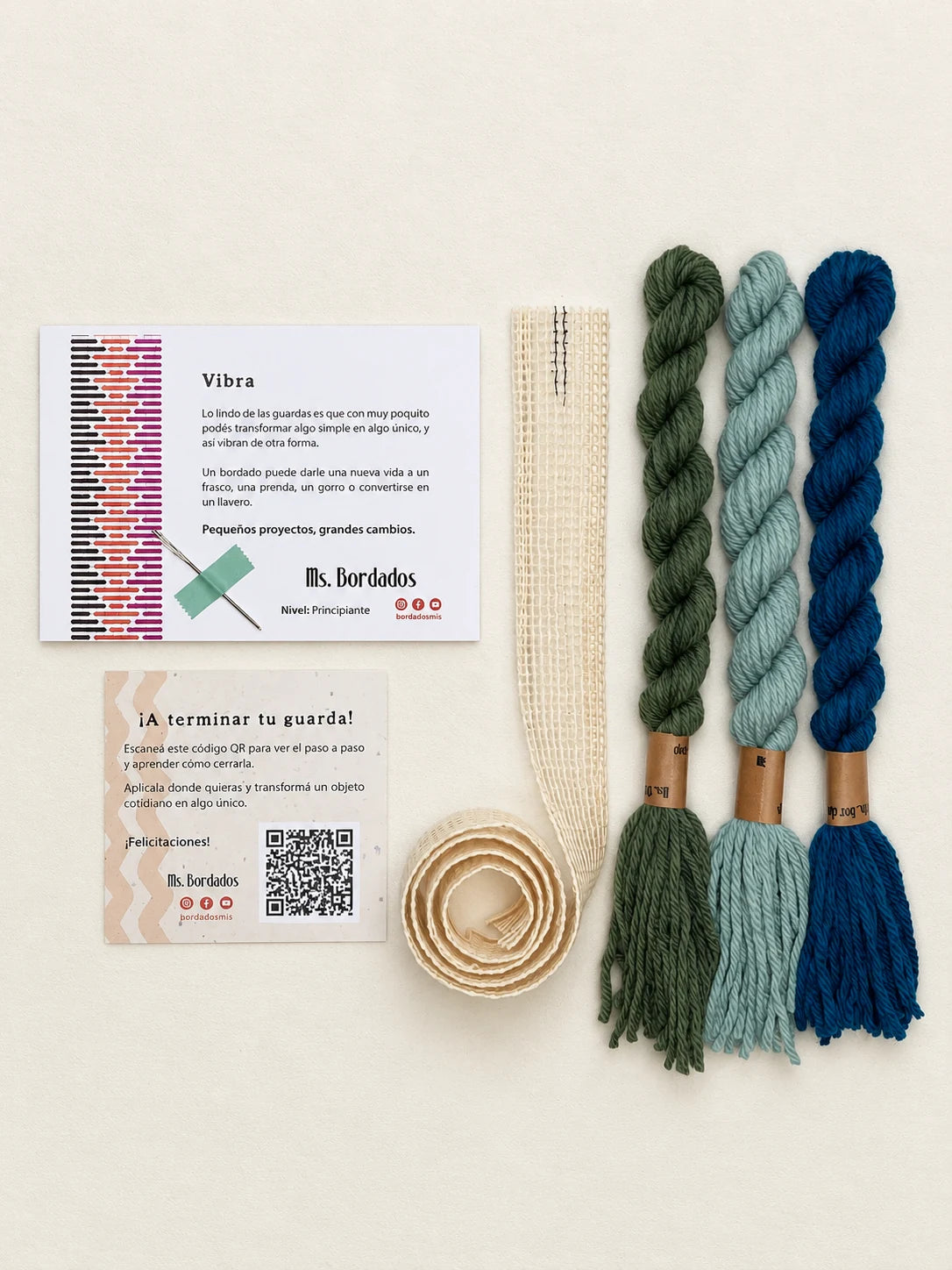 Componentes del Kit Franja Vibra Laguna (formato Guarda larga): cañamazo de 75 × 5 cm, lanas 100% uruguayas en Turquesa intenso, Celeste viejo y Verde bosque, aguja, manual impreso y tarjeta con el QR del video para terminar tu guarda — Ms. Bordados