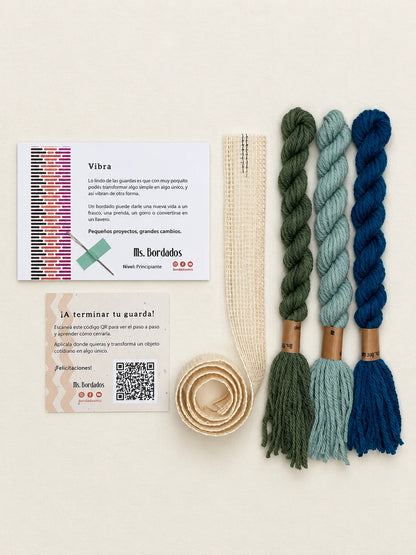 Componentes del Kit Franja Vibra Laguna (formato Guarda larga): cañamazo de 75 × 5 cm, lanas 100% uruguayas en Turquesa intenso, Celeste viejo y Verde bosque, aguja, manual impreso y tarjeta con el QR del video para terminar tu guarda — Ms. Bordados
