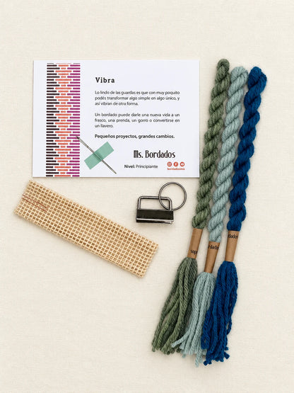 Componentes del Kit Franja Vibra Laguna (formato Llavero): cañamazo, lanas 100% uruguayas en Turquesa intenso, Celeste viejo y Verde bosque, aguja, manual impreso y herraje del llavero — Ms. Bordados