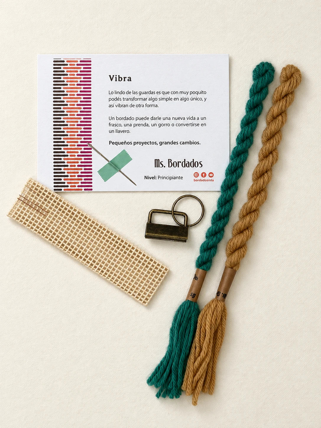 Componentes del Kit Franja Vibra Oliva (formato Llavero): cañamazo, lanas 100% uruguayas en Verde y Camel, aguja, manual impreso y herraje del llavero — Ms. Bordados